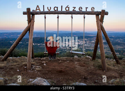 Eine Frau mit Sonnenhut und leichtem Schal genießt den Blick von einer Schaukel über die Stadt Alvaiazere in Zentralportugal Stockfoto