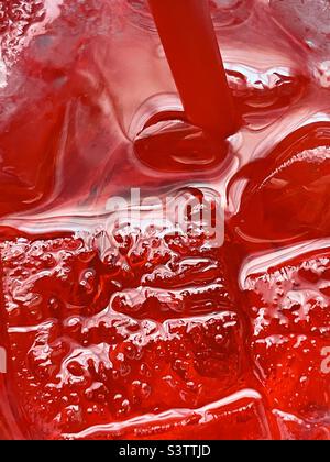 Blick hinunter in eine große Tasse eiskalten Kirschsprite. Die kalte rote kohlensäurehaltige Flüssigkeit, Stroh und Eis sorgen für eine tolle erfrischende Abstraktion. Stockfoto