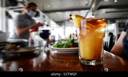 Mai Tai Cocktail mit orangefarbenem Segment, in einem kurzen Glas auf einer Theke, flacher Fokus, Salat im Hintergrund Stockfoto