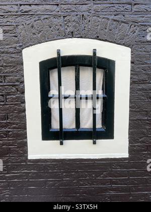 Kleines Fenster mit schmiedeeisernem Gitter im Zentrum von Amsterdam, Niederlande Stockfoto