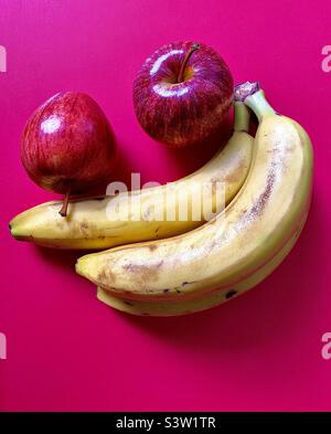 Zwei Rote Äpfel Und Drei Gelbe Bananen Auf Hellmagentafarbtem Snacktablett, Gesundes, Appetitliches Frisches Obst, Minimalistisch Stockfoto