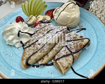 Blauer Teller mit Schokoladencrepes, frischem Obst und einer Kugel Vanilleeis Stockfoto