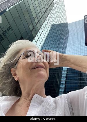 Eine weißhaarige Frau blickt auf Wolkenkratzer in New York City Stockfoto
