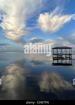 Große Abendwolken, die sich auf das ruhige Bay Water mit Boot und Dock spiegeln Stockfoto