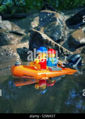 LEGO Figuren in einem roten Schlauchboot aus Gummi mit Außenbordmotor auf schlammigem Wasser Stockfoto