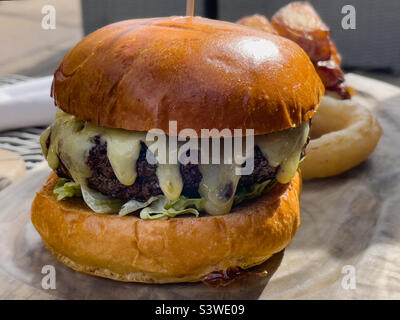 Cheeseburger mit geschmolzenem Käse und Zwiebelringen auf einer Holzplatte Stockfoto