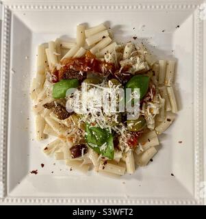 Nudelabend. Hausgemachte Tomatensauce, würzige Oliven, geröstete Artischocken, sonnengetrocknete Tomaten, Basilikum und Parmesan reggiano auf brauner Reisnudeln. Stockfoto