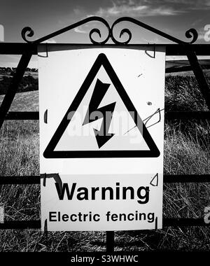 ‘Schockierend’ ein großes Schild warnt Eindringliche vor elektrischen Zäunen am Rande eines Bauernfeldes (Black & White) Stockfoto