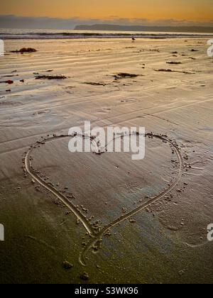 Liebe am Strand… Ein handgezeichnetes Herz liegt am goldenen Sand eines südkalifornischen Strandes, wenn die Sonne am Horizont untergeht. Stockfoto