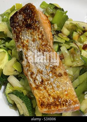 Knusprige Lachshaut auf Lachsfischfilet auf dem Bett aus sautierten Zucchini und Lauch Stockfoto