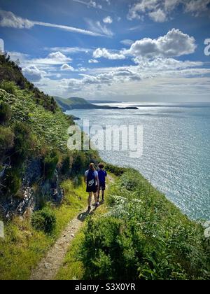 Eine Familie, die einen dramatischen Abschnitt des Ceredigion Coast Path in der Nähe von Llangrannog in West Wales entlang geht Stockfoto