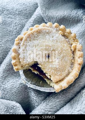 Bissen aus einem Mince Pie genommen, während sie in eine warme graue Decke eingewickelt…Weihnachten naht! Stockfoto