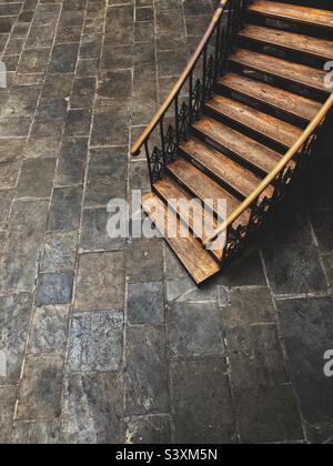Hi-Angle-Ansicht einer alten Holztreppe aus Eichenholz mit Geländern, die sich zu einem Steinkeller mit Kopierraum hinunterschlängeln Stockfoto