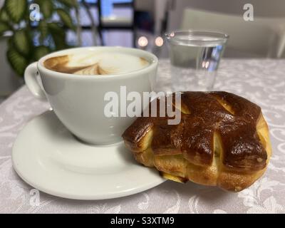 Frühstück in einer Bar mit einem Apfelcroissant, einer Tasse Cappuccino und einem Glas Wasser Stockfoto