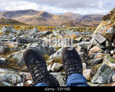 Blick auf die Füße und Lederstiefel der Wanderer auf dem Gipfel des Carn A’ Gheoidh, einem der Cairnwell Munros in Glenshee mit Blick auf Glas Tulaichean, Schottland Stockfoto