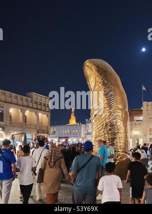 Die Goldene Daumenstatue, Souq Waqif, Doha, Katar, mit dem Islamischen Kulturzentrum Fanar Qatar im Hintergrund Stockfoto