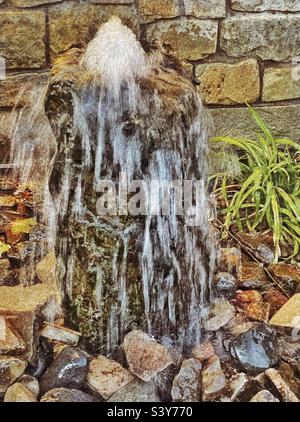 Ein kleiner dekorativer Wasserbrunnen auf dem Gelände des Gardner Village im Salt Lake Valley von Utah, USA. Der sprudelnde Brunnen und der Wasserfluss wurden in der Kamera eingefroren, was interessante Muster hervorgebracht hat. Stockfoto