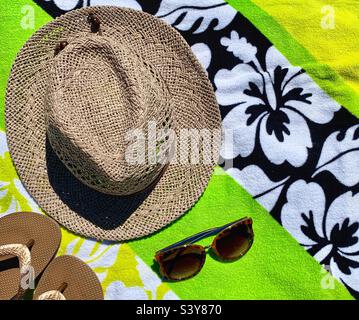 Ein brauner Hut, Sonnenbrille und Hausschuhe auf den Strandhandtüchern Stockfoto