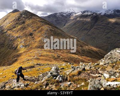 Weibliche Walker auf dem Pfad und schneebedeckten Hängen von Munro Buachaille Etive Beag, Glencoe, Schottland Stockfoto