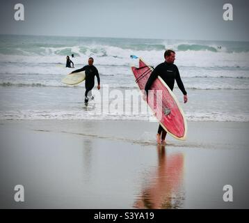 Zwei Surfer kommen aus dem Meer und tragen ihre Surfbretter am Saunton Sands in North Devon in England Stockfoto