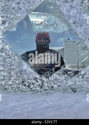 Frischer Schnee und Eis wurden von einem Seitenfenster auf der Beifahrerseite abgekratzt, nachdem über Nacht in diesem Viertel in Utah, USA, starker Schneefall aufgetreten war, was zu einem unbeabsichtigten Selfie in Fensterglasspiegelung führte. Stockfoto