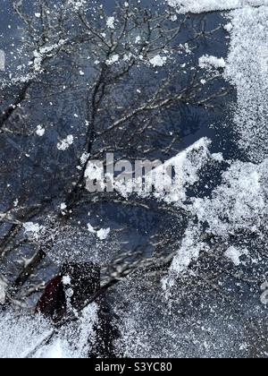 Neuschnee und Eis wurden von der Windschutzscheibe eines SUV geschabt, nachdem über Nacht in diesem Viertel in Utah, USA, starker Schneefall aufgetreten war. Kühle Abstraktion aus Reflexionen in Glas- und Schneepartikeln. Stockfoto