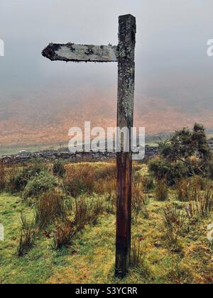 Uralte, mit Moos und Flechten bedeckte Wegweiser für Wanderer in der abgelegenen und verlassenen Landschaft von Dartmoor im Nebel während des Winters in Devon England Stockfoto