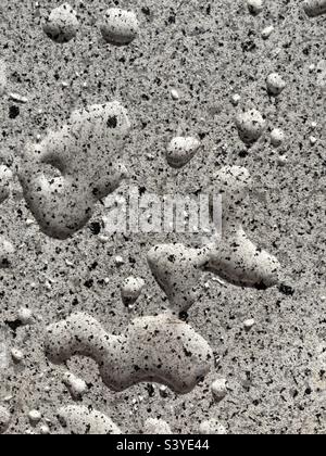 Wassertropfen auf einer grauen Oberfläche mit gesprenkelten schwarzen Punkten Stockfoto