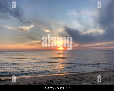 Am Meer scheint die rot-goldene Sonne hinter den Wolken, bevor sie untergeht Stockfoto