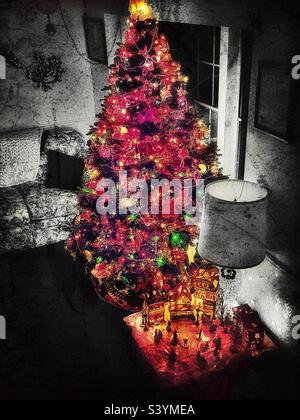 Ein abgedunkeltes Wohnzimmer in einem Haus in Utah, USA, gefüllt nur mit dem glühenden Bernsteinlicht des beleuchteten Weihnachtsbaums und anderen Weihnachtsdekorationen. Grunge digital hinzugefügt für einen Vintage-Look. Stockfoto