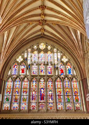 Unglaublich helle und farbenfrohe riesige Buntglasfenster, die Heilige und religiöse Szenen in einem kunstvoll geschnitzten Steinfensterrahmen mit architektonischen Details in der Kathedrale von Exeter darstellen Stockfoto