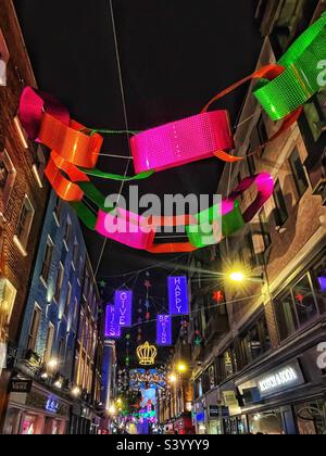 Weihnachtslichter in Form einer riesigen Papierkette auf der schmalen Soho Street in London, die das Nachtleben und den Stadtteil für festliche Feierlichkeiten fördern - Beleuchtung und Farbe in den Wintermonaten Stockfoto