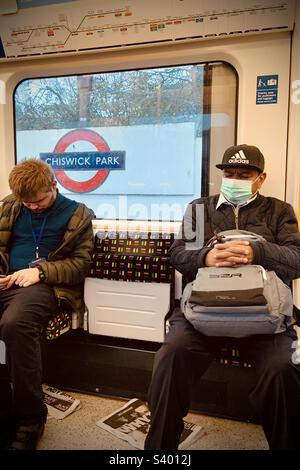 Zwei Männer schlafen in einem Londoner U-Bahn-Zug an der Chiswick Park Station. Ein Mann trägt eine Gesichtsmaske. Stockfoto