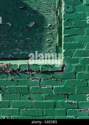 Grün bemalte Backsteinwand mit verkleidetem Fenster. Stockfoto