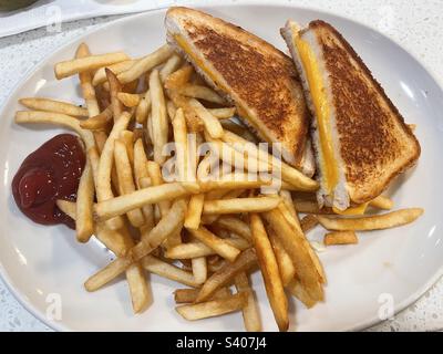 Ein großer weißer Teller mit einem gegrillten Käsesandwich und pommes frites Stockfoto
