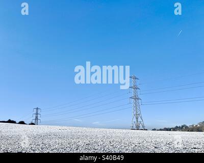 Gefrorenes Feld bedeckt mit Schnee an einem hellen und klaren Dezembertag mit Strommasten. Winter in Kent Countryside, England Stockfoto