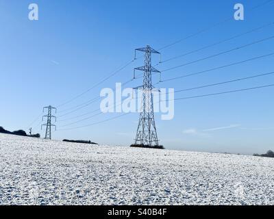 Gefrorene, schneebedeckte Felder mit Strommasten an einem kalten Wintermorgen im Dezember in Kent, England, 2022. Stockfoto