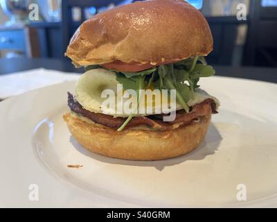 Perfektes sonniges Frühstückssandwich mit Eiern und Speck mit Tomaten, Rucola und scharfen Aioli Stockfoto