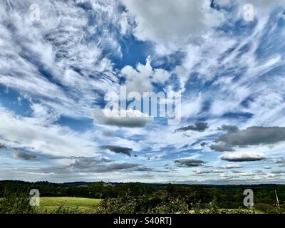 Cirrus und Cumulus Wolken verstreut über einem blauen Himmel im Sommer über grünen Feldern, Somerset, England, Großbritannien Stockfoto