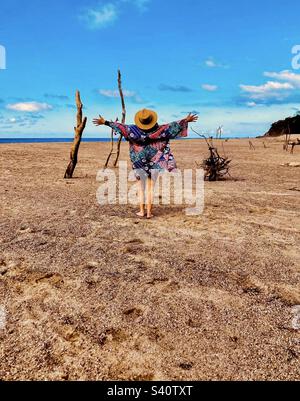 Eine Frau mit ausgestreckten Armen nimmt die erstaunliche Natur des Lo De Marcos Strandes auf. Stockfoto