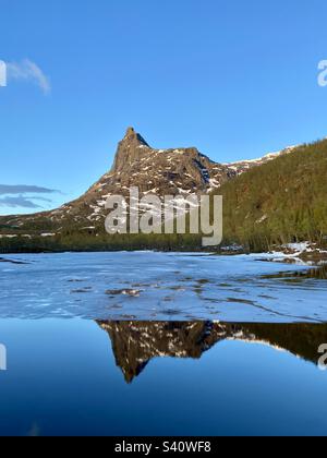 Blick auf den Berg Romabstøtta in Nordnorwegen über dem Wasserreservoir mit noch etwas Eis drauf. Spiegeleffekt im Wasser vom Berggipfel. Foto während der Wanderung gegen Mitternacht. Stockfoto