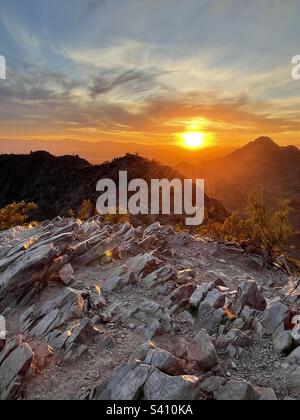 Ein wunderschöner goldener Sonnenuntergang lässt Licht zwischen den Phoenix Mountain Preserve Peaks fließen, die von den angewinkelten Felsen des Two Bit Peak glitzern und den Rand der Kreosotbüsche in Scottsdale, AZ, erstrahlen Stockfoto