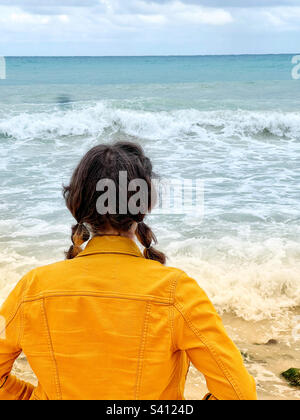 Junge Frau in gelber jeansjacke, die auf das Karibische Meer in Mayan Riviera, mexiko schaut Stockfoto