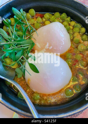 Nahaufnahme einer Schüssel mit grüner Erbsensuppe mit zwei langsam gekochten pochierten Eiern mit Mikrogrünem, fotografiert von oben Stockfoto