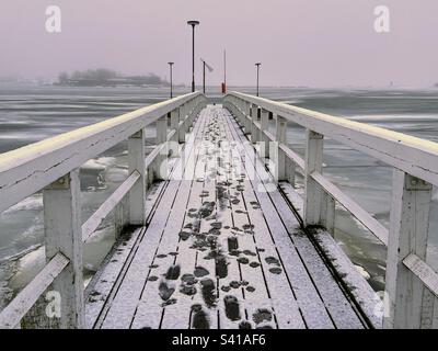 Hölzerne Wanderbrücke mit Fußspuren im Schnee über der Ostsee Stockfoto