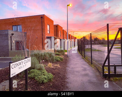 Einen Pfad mit Stadthäusern entlang zu laufen, auf der einen Seite ein Zaun auf der anderen Seite bei Sonnenuntergang. Stockfoto