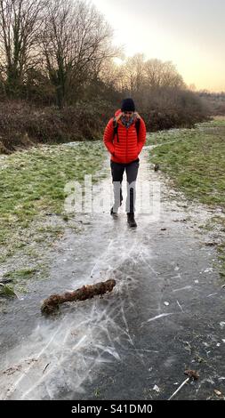 Eine Frau in einer orangefarbenen Jacke läuft vorsichtig auf Eis in Großbritannien Stockfoto