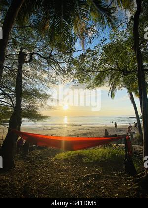 Eine orangefarbene Hängematte hängt zwischen zwei Palmen, während die Sonne bei Nosara in Costa Rica untergeht Stockfoto