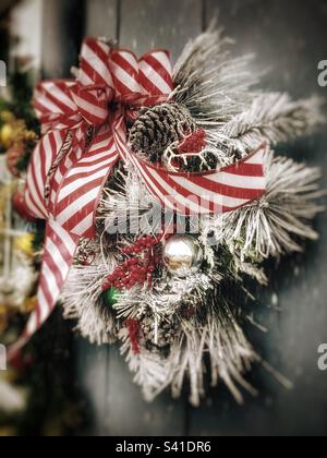 Festlicher Weihnachtskranz mit roter und weißer Schleife, die an einer Tür hängt Stockfoto