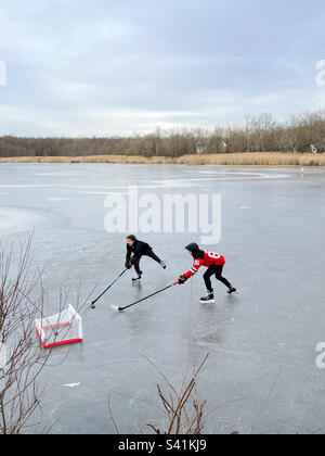 Zwei Jungs spielen Eishockey auf einem gefrorenen Teich in New Jersey, USA. Stockfoto